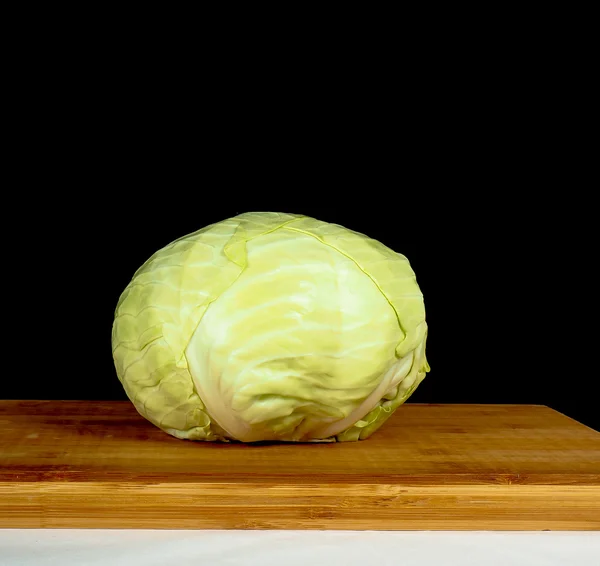 Ganzer Kohl isoliert in Richtung Schwarz, auf einem Holzschneidebrett — Stockfoto