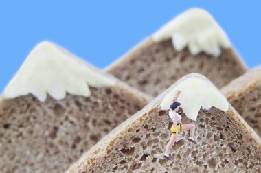 A  toy mountaineer on mountains, made of healthy rye bread and creamy cheese. Ecotourism and healthy eating concept. clipart