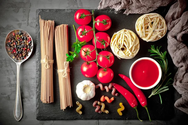 stock image Pasta in a composition with vegetables and kitchen accessories on an old background