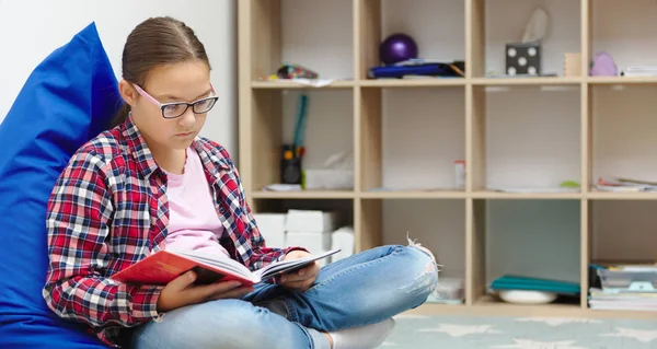 女の子は本を読んでいる間に部屋に座って — ストック写真