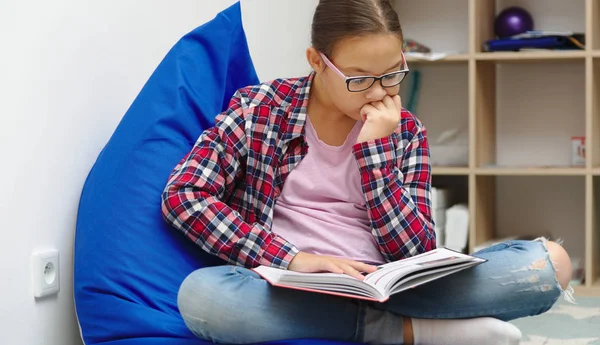 Dívka čte knihu, zatímco sedí v pokoji — Stock fotografie