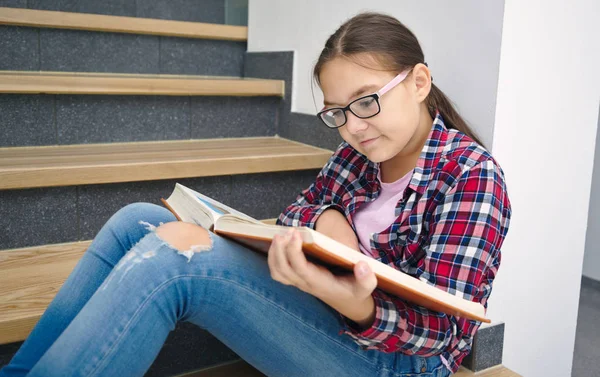 Девушка читает книгу, сидя на лестнице — стоковое фото