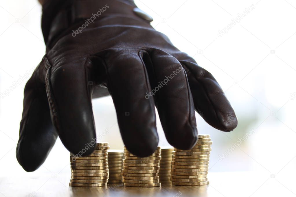 Stealing money - Greedy hand with black gloves grabbing or reaching out for pile of golden coins. Close up - Concept for tax, fraud and greed
