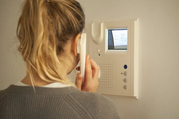 Sarışın kadın Crt ekranındaki ekrana bakarken kapı telefonuna cevap veriyor. Video dahili iletişim cihazları. Seçici odak resmi.