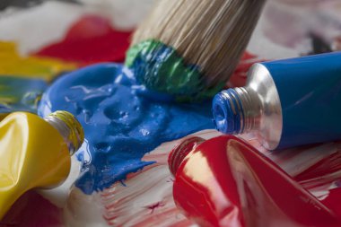 Boya fırçasının etraftaki boya tüpleriyle sanatçı paletinden mavi renk seçerken yakın plan. Bir sanatçı stüdyosundan ya da yaratıcı eğitim veren bir okuldan renkli bir görüntü. Fırçada hareket bulanıklığı.