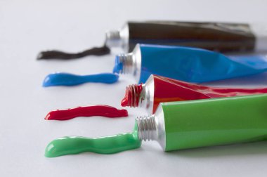 Bir sırada duran yeşil, kırmızı, mavi ve siyah renkli boya tüplerini kapatın. Tüplerden renkli çizgiler çıkıyor. Bir sanatçı stüdyosundan ya da yaratıcı eğitim veren bir okuldan renkli bir görüntü. Seçici odak.