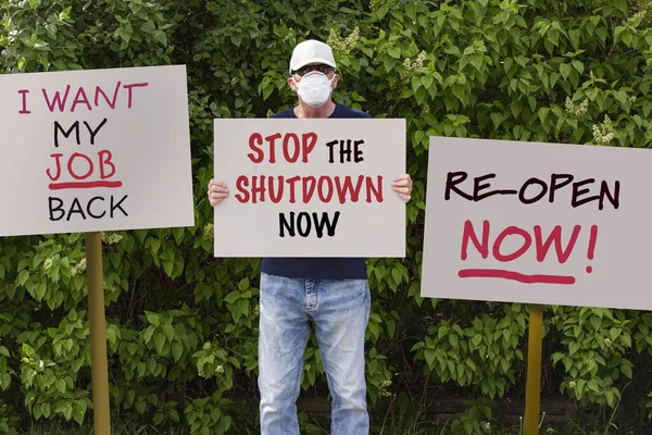 由于Covid 19流感大流行 戴帽子和戴医疗保护面具的抗议者举行示威 抗议留在家中的命令 并在示威中张贴了 立即停止关闭 的标语 更多的标志板围绕着他 — 图库照片