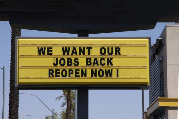Billboard saying We Want Our Jobs Back Open up Now! With palm trees and blue sky background. Anti-lockdown protests.