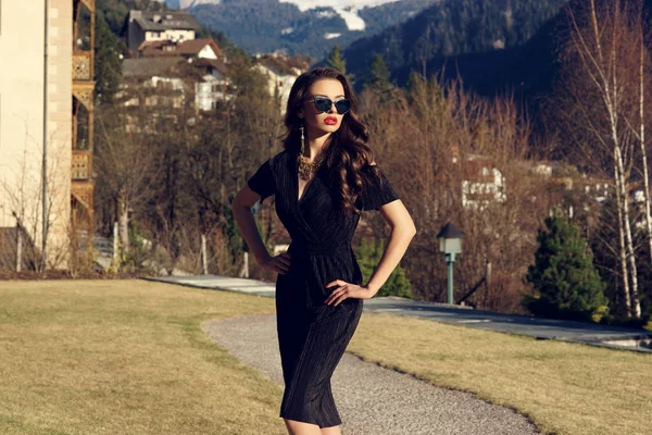 有魅力的女人，穿着构成对山背景上的黑色连衣裙 图库图片