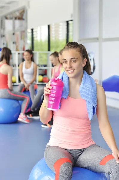 Schöne junge Frau sitzt auf dem blauen Pilates-Ball und lächelt. Gruppe von Sportlerinnen, die hinten sitzen. — Stockfoto