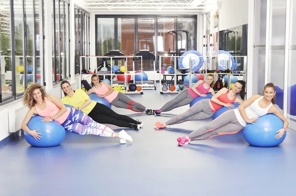 Grupo de hermosas mujeres jóvenes haciendo ejercicio en bolas de pilates azules y sonriendo — Foto de Stock