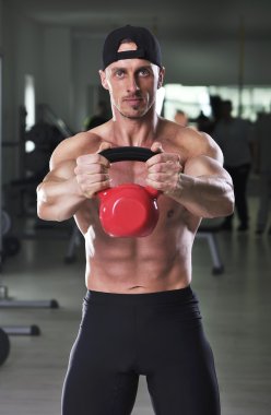 Su ısıtıcısı çan ile omuz egzersiz yapan yakışıklı güçlü atletik erkek. Mükemmel kaslı abs, kollar ve göğüs ile güçlü vücut geliştirmeci.