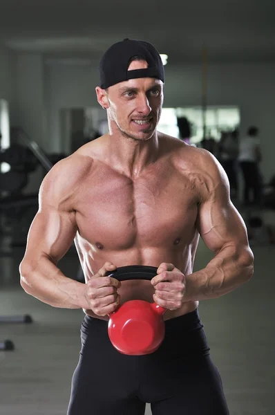 Handsome powerful athletic man doing biceps exercise with kettle bell. Strong bodybuilder with perfect muscular abs, arms and chest. — Stock Photo, Image