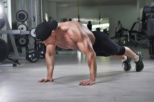 Knappe krachtige atletische man uitvoeren push-ups op de sportschool. Sterke bodybuilder met perfecte rug, schouders, biceps, triceps en borst. — Stockfoto