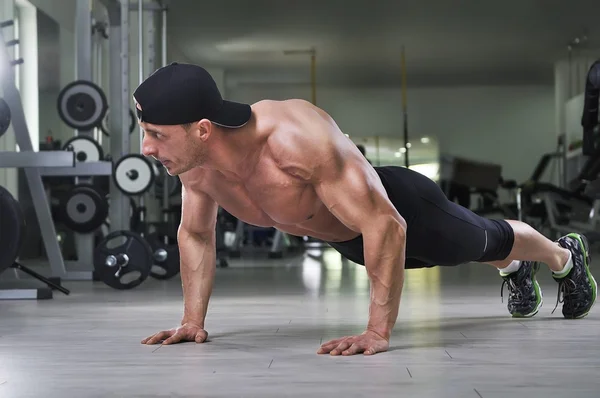 Knappe krachtige atletische man uitvoeren push-ups op de sportschool. Sterke bodybuilder met perfecte rug, schouders, biceps, triceps en borst. — Stockfoto