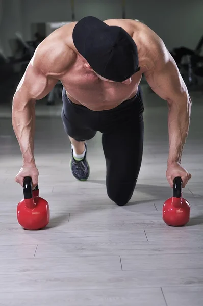 Vacker kraftfull atletisk man utför armhävningar med panna ringklocka. Stark kroppsbyggare med perfekt axlar, biceps och triceps. — Stockfoto