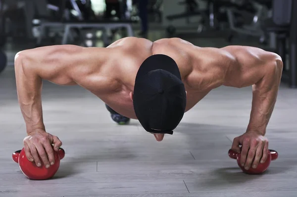 Vacker kraftfull atletisk man utför armhävningar med panna ringklocka. Stark kroppsbyggare med perfekt axlar, biceps och triceps. — Stockfoto