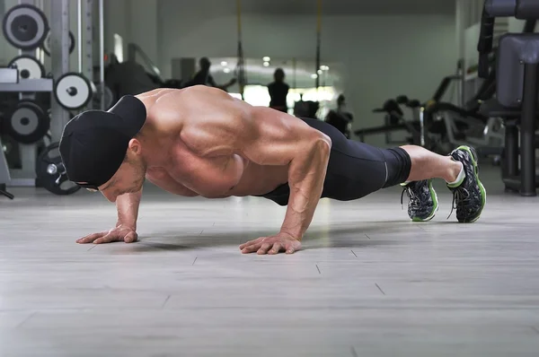 Knappe krachtige atletische man uitvoeren push-ups op de sportschool. Sterke bodybuilder met perfecte rug, schouders, biceps, triceps en borst. — Stockfoto