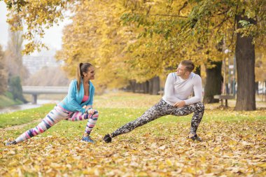 Güzel genç çift birlikte germe ve hazırlama parkta çalıştırın. Sonbahar çevre.