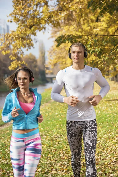 Schönes junges Paar, das Musik hört und zusammen im Park läuft. Herbstliches Umfeld. — Stockfoto