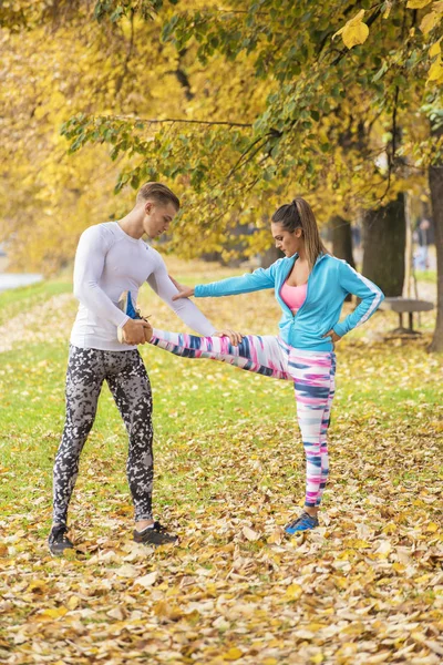 Hermosa pareja joven estirándose juntos y preparándose para correr en el parque. Ambiente otoñal . — Foto de Stock