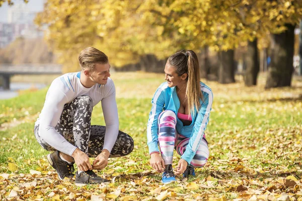 Schönes junges Paar, das seine Schuhe für den Lauf im Park vorbereitet. Herbstliches Umfeld. — Stockfoto