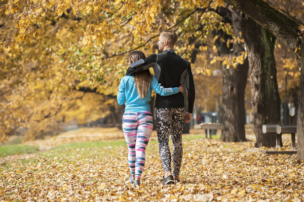 Beautiful young couple walking together in the park. Back view. Autumn environment.