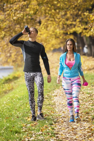 Belo jovem casal se refrescando depois de correr no parque. Ambiente de Outono . — Fotografia de Stock