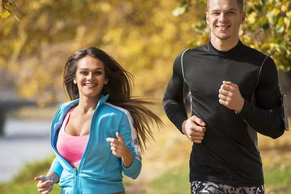 Hermosa pareja joven corriendo juntos en el parque. Ambiente otoñal . — Foto de Stock