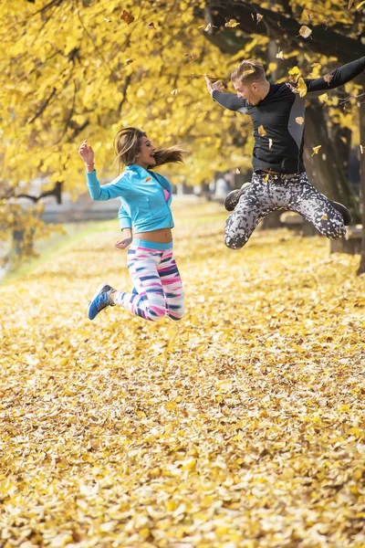 Hermosa pareja joven celebrar y saltar después de un entrenamiento exitoso en el parque. Ambiente otoñal . — Foto de Stock