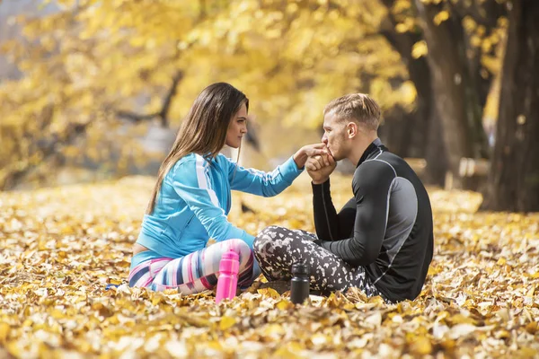 Schönes junges Paar, das sich nach dem erfolgreichen Training im Park ausruht und küsst. Herbstliches Umfeld. — Stockfoto