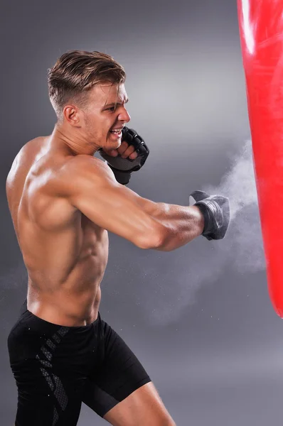 Muskulöser Kämpfer, der einige Tritte mit Boxsack übt. Boxen auf grauem Hintergrund. das Konzept eines gesunden Lebensstils — Stockfoto