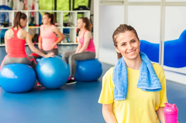 Mulher bonita sentada na bola pilates azul e sorrindo. Grupo de atletas do sexo feminino sentadas atrás . — Fotografia de Stock