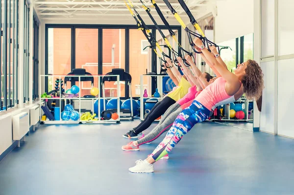 Group of beautiful young women working out on TRX and smiling. — Stock Photo, Image