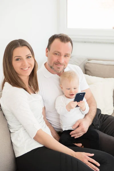 3 행복 한 가족을 집에서 즐기고 있습니다. 부모와 그들의 아름 다운 아기 여자는 소파에 앉아서 카메라를 보고 가족 값 합니다. 함께 여가. 스톡 사진