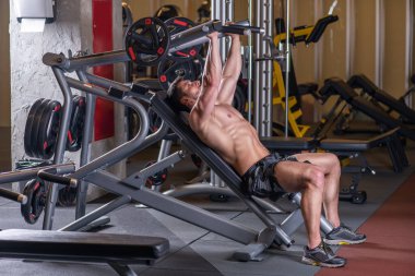 Makinede göğüs egzersizi yapan seksi kaslı genç adam. Yan görünüm