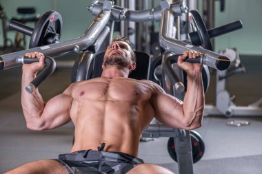 Makinede göğüs egzersizi yapan seksi kaslı genç adam. Ön görünüm