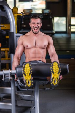 Seksi kaslı adam makinede bacak esnetme egzersizi yapıyor ve bağırıyor.