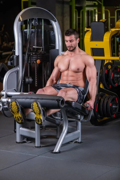 Sexy muscular man doing leg extension exercise on the machine
