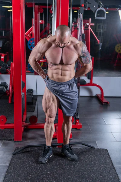 Powerful muscular man posing with upper leg muscle contraction at the gym