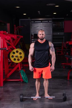 Güçlü kaslı adam spor salonunda halterle pazı egzersizi yapmaya hazırlanıyor.