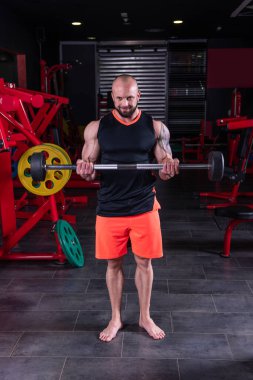 Güçlü kaslı adam spor salonunda halterle biceps egzersizi yapıyor.
