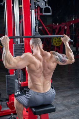Güçlü kaslı adam, Lat makinesinde egzersiz yapıyor.
