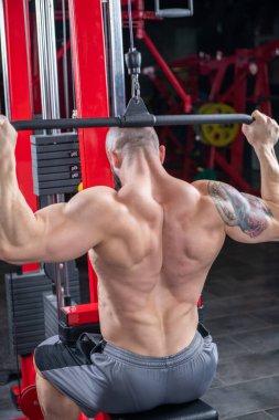 Güçlü kaslı adam, Lat makinesinde egzersiz yapıyor.