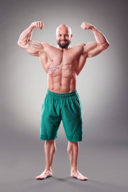 Gri arka planda seksi kaslı vücut bulucu pozu