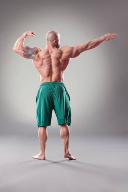 Gri arka planda poz veren seksi kaslı vücut bulucu. Arka plan