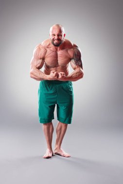 Gri arka planda seksi kaslı vücut bulucu pozu