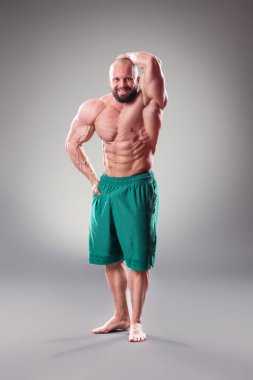 Gri arka planda seksi kaslı vücut bulucu pozu