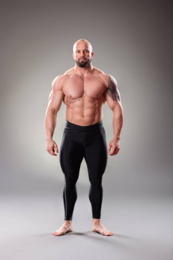 Gri arka planda seksi kaslı vücut bulucu pozu