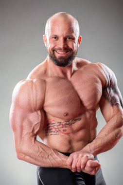 Gri arka planda poz veren seksi kaslı vücut bulucuyu kapat